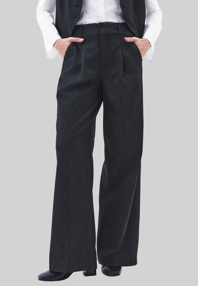 Zwarte pantalon met krijtstreep, gemaakt van een gestructureerde stof, met een hoge taille, brede pijpen en zijzakken, gecombineerd met zwart schoeisel.