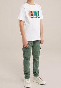 Vit Minecraft-temat t-shirt med färgglada block och figurer, i kombination med gröna cargobyxor med sidofickor och vita sneakers.