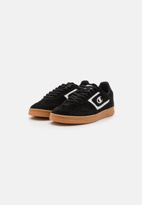 Tenisi din suede negru cu un logo alb, având șirete negre și o talpă din cauciuc colorat, având un design low-top și un finisaj texturat.