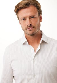 Camisa de botones de color claro y rayas con cuello extendido, hecha de una tela suave, con un corte ajustado y botones transparentes.