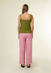 Grön stickad ärmlös topp med fyrkantig halsringning, tillsammans med rosa blommiga vida byxor. Klädselen har horisontella och vertikala mönster.