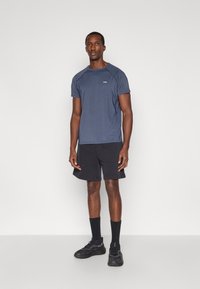 Ναυτικό μπλουζάκι απόδοσης με ραγλάν μανίκια, σε συνδυασμό με μαύρα σορτς. Το σύνολο περιέχει ένα λογότυπο στη μπλούζα και μαύρα αθλητικά παπούτσια.