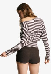 Prugasti dugi rukav majica u smešnim i krem nijansama s off-the-shoulder dizajnom, uparen s tamnim šortsevima. Tekstura izgleda meka i ležerna.