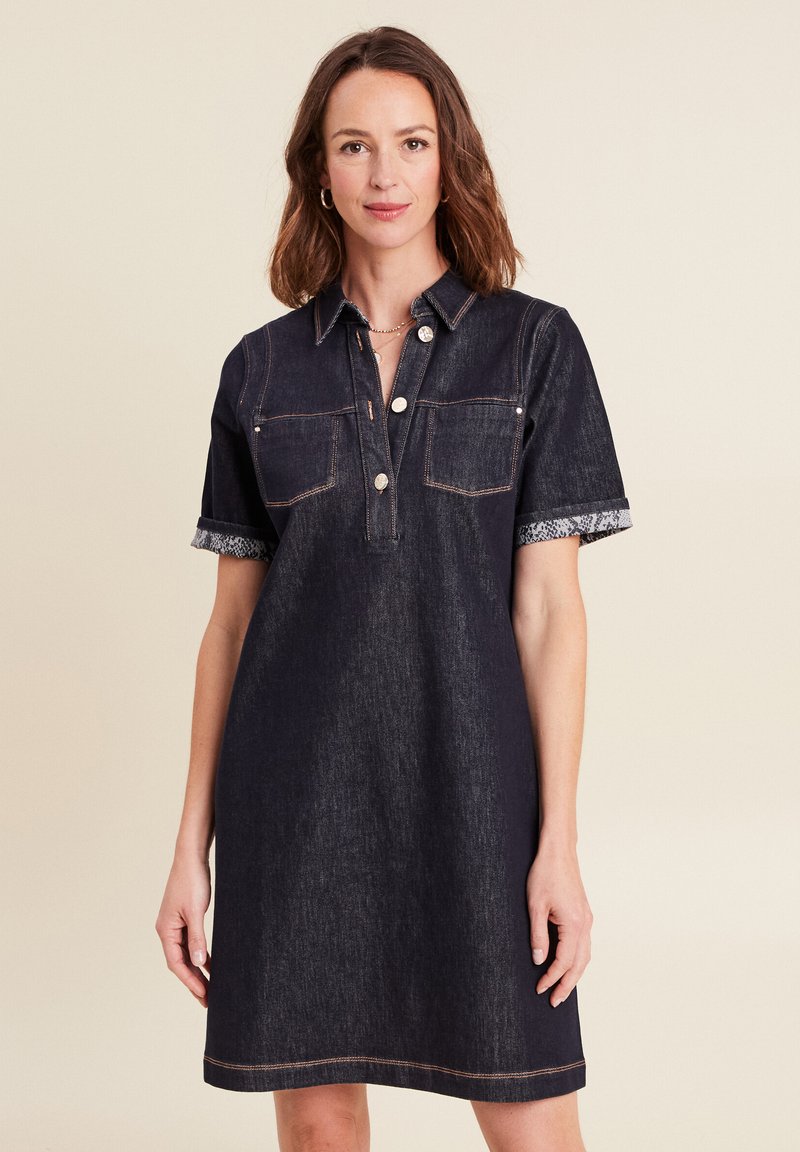 Robe en denim foncé à manches courtes, avec deux poches poitrine et un plastron à boutons. Elle présente des poignets à motif serpent contrastant et des coutures orange.