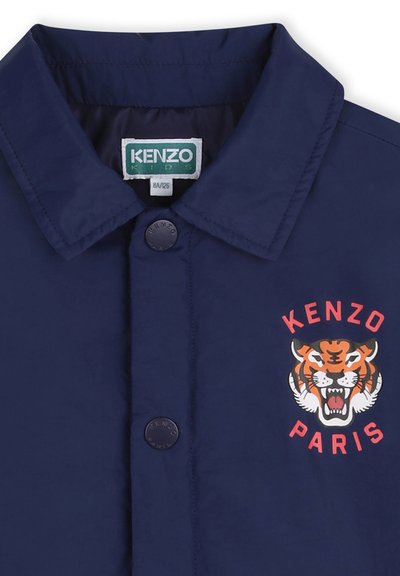 Marineblauwe jas met een puntige kraag, voorzien van een circulair oranje-wit tijgerlogo en de tekst 'KENZO PARIS'. De knopen zijn donker en rond.