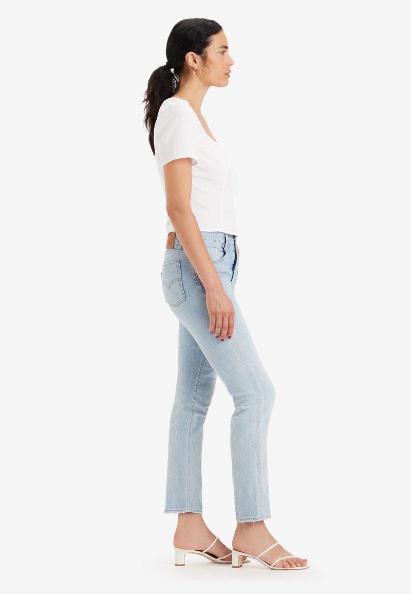 Jean en denim bleu clair avec une coupe droite et un ourlet effiloché, associé à un haut blanc à manches courtes et des sandales à talons crèmes.