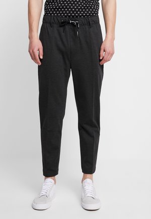 Czarne, dopasowane spodnie dresowe z troczkiem w pasie, noszone z białymi sneakersami i czarną koszulą w wzory.