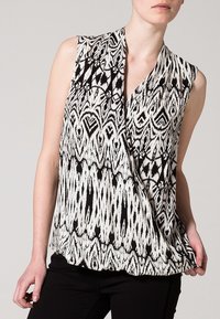 Czarna i biała bezrękawnik z geometrycznym wzorem, projekt z dekoltem w kształcie litery V oraz zwiewną sylwetką, wykonany z lekkiego materiału.