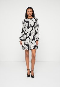 Melnas kleitas ar baltu lapu rakstu, garām piedurknēm, apaļu kakla izgriezumu un brīvu piegriezumu, kas krīt virs ceļgaliem. Valkā ar melniem potīšu siksniņu zābakiem.