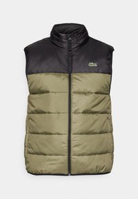Gilet rembourré, présentant une partie supérieure noire et une partie inférieure vert olive. Fermeture éclair à l'avant, col haut et petit logo. Texture lisse.