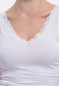 White V-neck top featuring a delicate lace trim around the neckline, made from soft fabric with a smooth texture and fitted design.