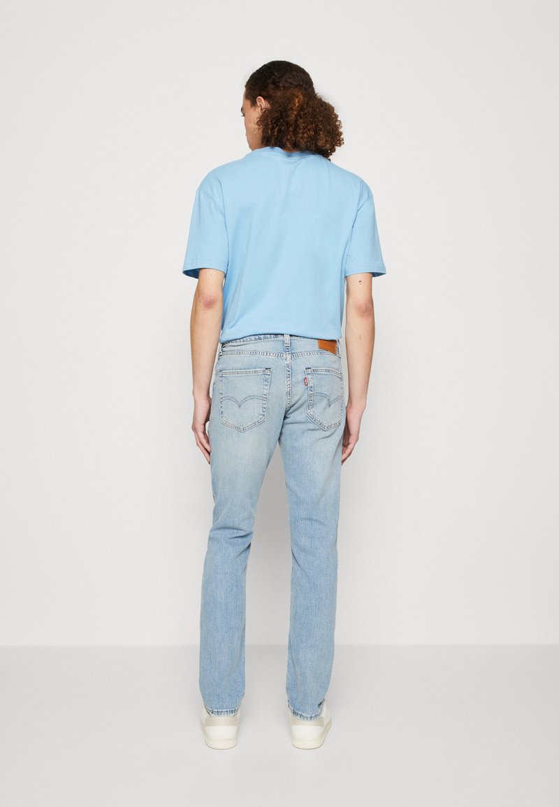 T-shirt azzurro chiaro a maniche corte e jeans in denim chiaro, con taglio dritto, patch del brand discreto e sneakers bianche.