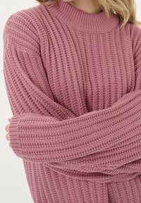 Różowy sweter z dzianiny z pionowymi prążkami, wysoka szyja i długie rękawy. Miękka faktura, z luźnym krojem i ściągaczami na rękawach.