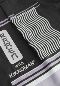 Čierna látka s grafickou potlačou, na ktorej sú v tučnom bielom a sivom písme slová "RAREN", vlnité čiary a fialový pruh, značkované spoločnosťou Kikkoman.