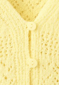 Gros plan sur un tissu tricoté jaune doux avec deux boutons ronds assortis le long de la bande à boutons côtelée.