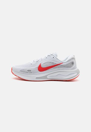 White mesh athletic shoes with red accents, featuring a prominent red Nike swoosh, textured upper, and grey sole.