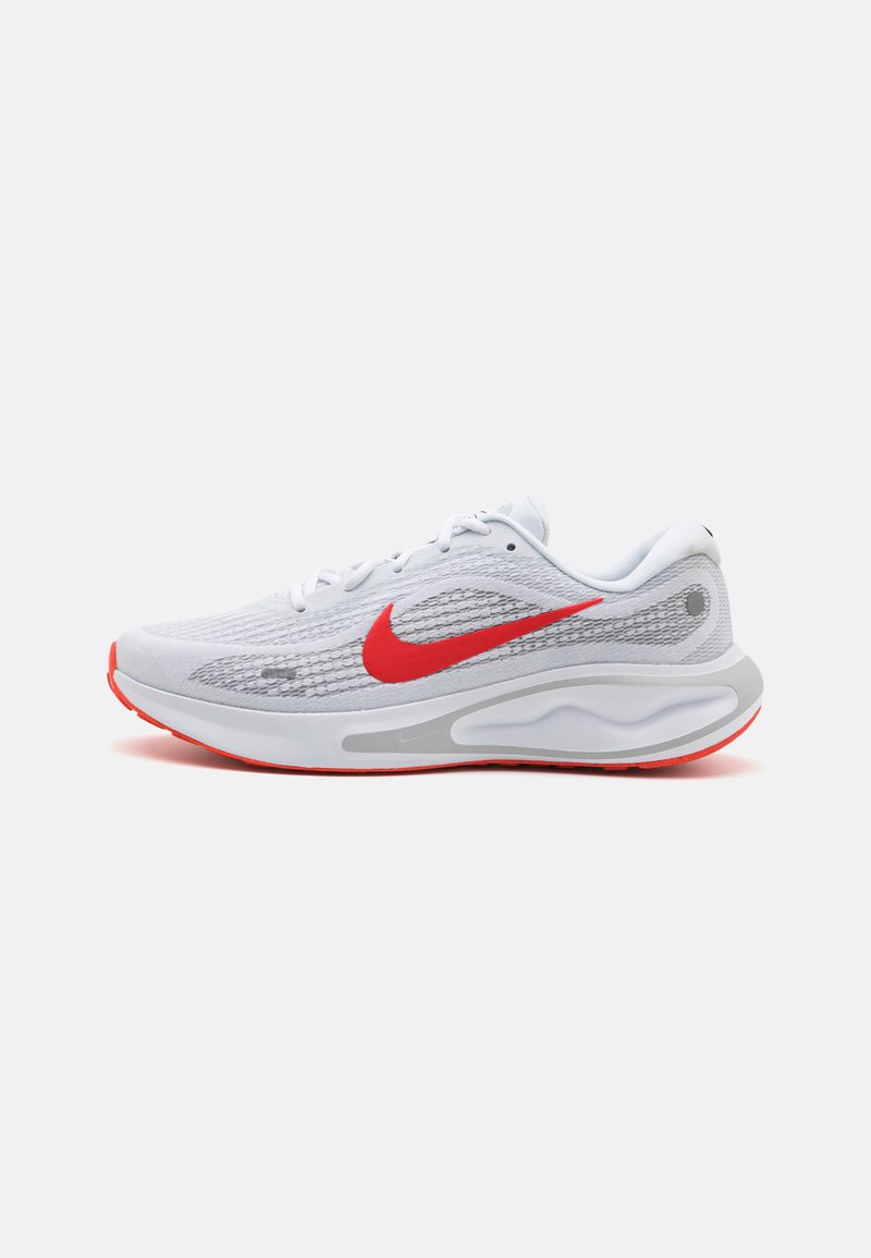 Hvite mesh sportssko med røde accenter, med en fremtredende rød Nike-swoosh, teksturert overdel og grå såle.