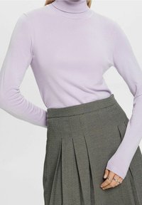 Hellblauer Rollkragenpullover aus weichem Strickstoff, kombiniert mit einem grauen Rock, der ein dezentes geometrisches Muster und einen plissierten Schnitt aufweist.