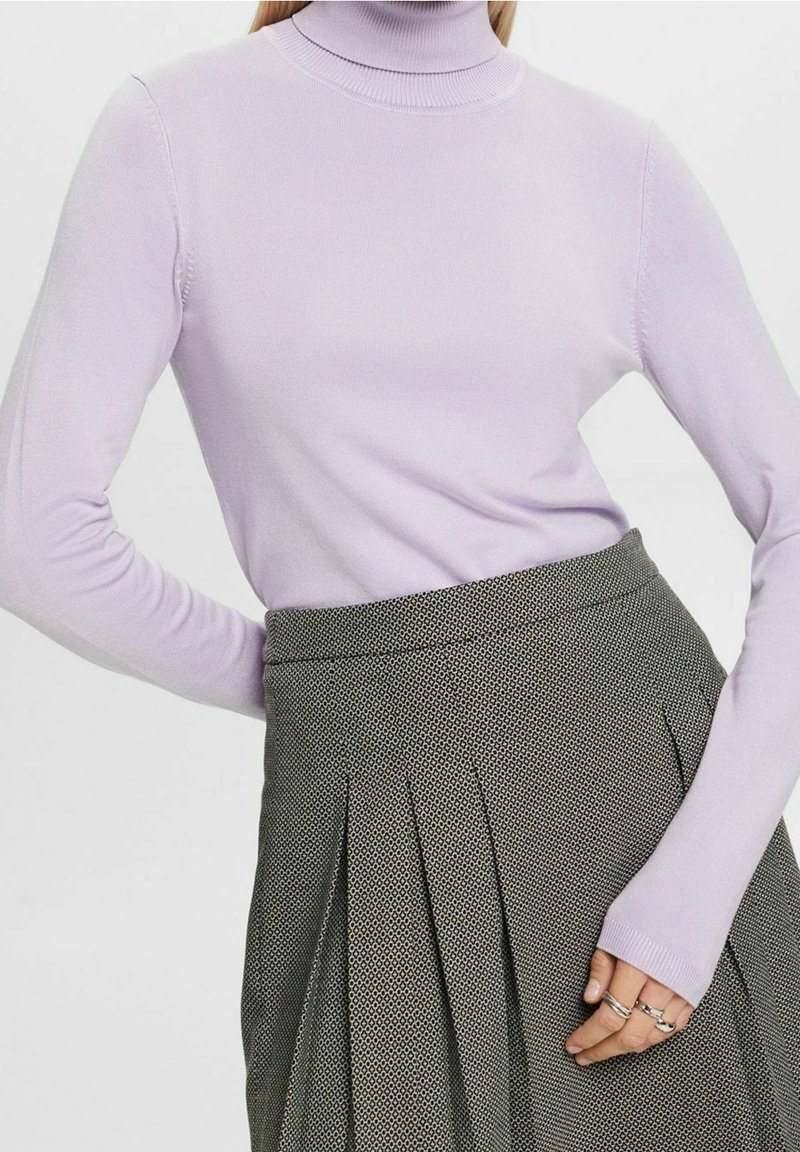 Hellblauer Rollkragenpullover aus weichem Strickstoff, kombiniert mit einem grauen Rock, der ein dezentes geometrisches Muster und einen plissierten Schnitt aufweist.