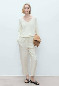 Krämfärgad stickad tröja med V-ringning, ihopparad med ljusbeige byxor med dragsko. Outfits kompletteras av gråa sandaler med öppet tå.