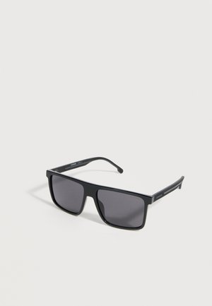 Μαύρα ορθογώνια γυαλιά ηλίου με σκουρόχρωμους φακούς και ελαφρώς κυρτά πλαϊνά που ακουμπούν σε μια ανοιχτόγριζη επιφάνεια.