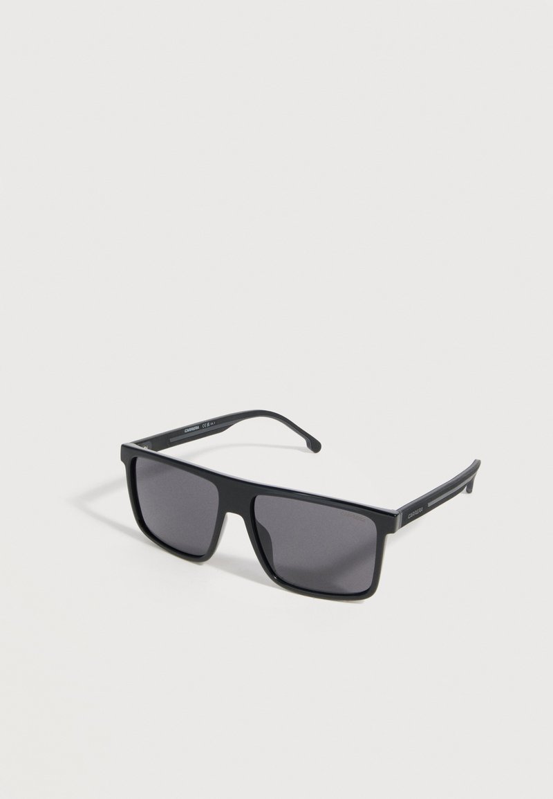 Μαύρα ορθογώνια γυαλιά ηλίου με σκουρόχρωμους φακούς και ελαφρώς κυρτά πλαϊνά που ακουμπούν σε μια ανοιχτόγριζη επιφάνεια.