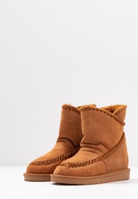 Bottines en suède beige avec un design plié, des coutures décoratives et une doublure intérieure chaude, présentant une semelle en caoutchouc plate.