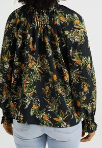 Černá květinová blůza se vzory v oranžové a zelené barvě, obsahující nařasený výstřih, dlouhé rukávy a strukturovanou tkaninu.