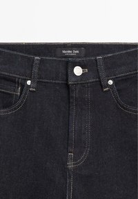 Dunkelblaue Denim-Jeans mit geradem Schnitt, goldenen Nähten, einem Metallknopfverschluss und einem Markenetikett am Bund.