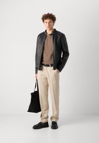 Chaqueta de cuero negra, camiseta marrón, pantalones de lino beige, cinturón negro, zapatos negros, bolsa tote negra; texturas suaves y colores neutros.