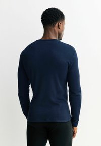 Navy blue long-sleeve shirt made from knit fabric, featuring a round neckline and a fitted design. The back is smooth with no visible patterns.
