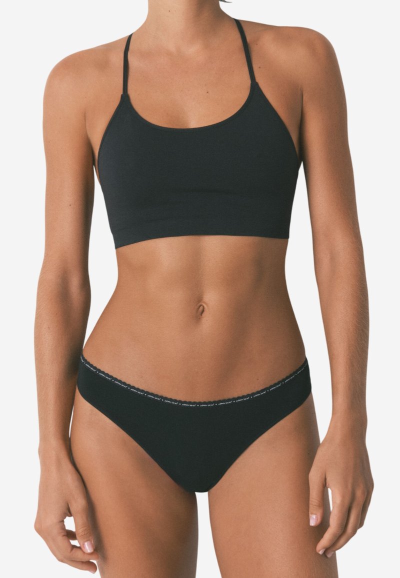 Schwarze Bralette mit dünnen Trägern, glatter Textur und rundem Ausschnitt. Passende schwarze Bikini-Höschen mit einem kontrastierenden Bunddetail.