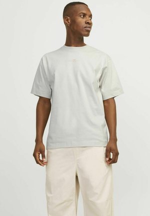 Lichtgrijze katoenen t-shirt met korte mouwen en een ronde hals. Bevat subtiele bedrukte tekst aan de voorkant, gecombineerd met crèmekleurige broeken.