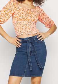 Orange floral crop top with puffed sleeves; paired with a dark denim skirt featuring a tied belt and a front slit.