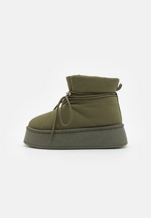 Olive green mid-calf boot with padded fabric and lace closure, featuring a platform sole and quilted texture details.