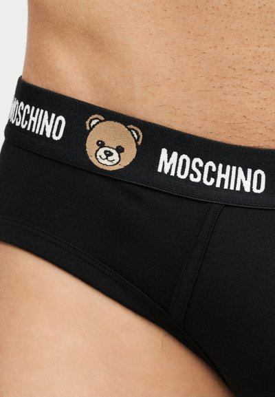Μαύρη μέση εσωρούχου με το λογότυπο Moschino και μια καρτούν αρκουδίτσα στο πλάι, φορεμένο σε ανδρικό κορμό με ανοιχτόχρωμο δέρμα.