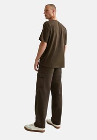 Bruine T-shirt met een relaxte pasvorm, gecombineerd met bruin cargobroek met zijzakken en een rechte pijp, aangevuld met witte sneakers.