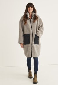 Gray fleece coat with a high collar, featuring black fabric accents and two front pockets. The design is oversized with long sleeves.