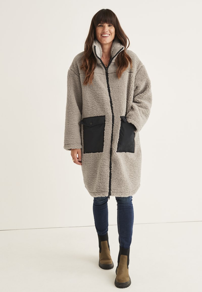 Gray fleece coat with a high collar, featuring black fabric accents and two front pockets. The design is oversized with long sleeves.