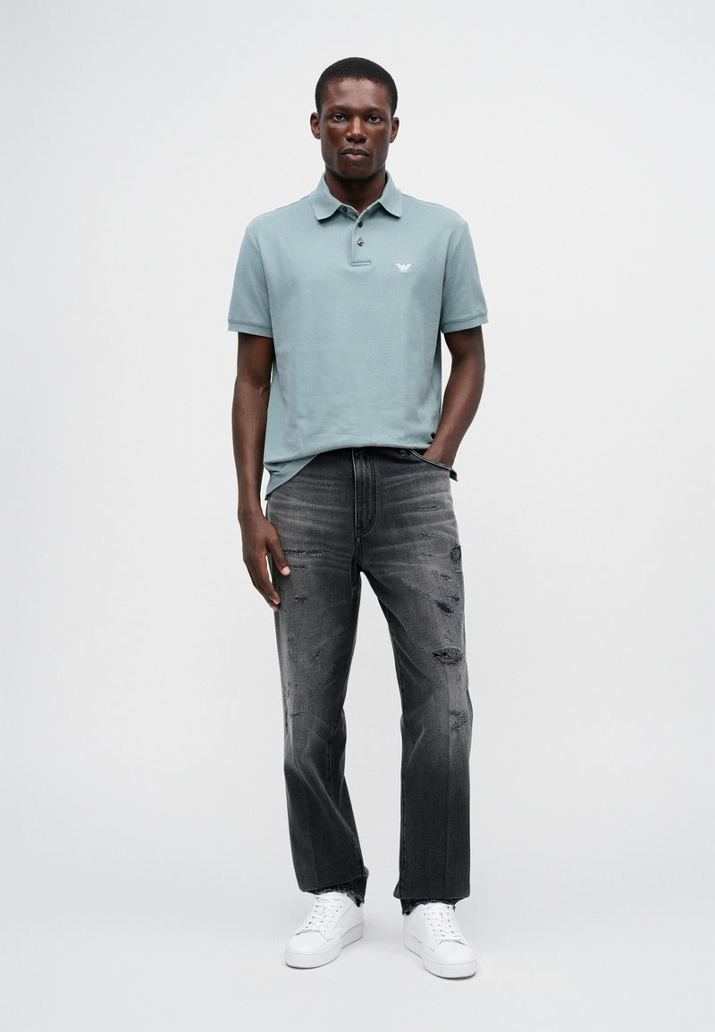 Polo en coton mélangé vert clair, avec un col et des manches courtes. Porté avec un jean noir déchiré et des baskets blanches.