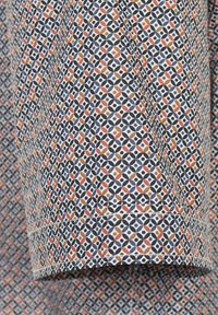 Tkanina bawełniana z geometrycznym wzorem w odcieniach granatu, pomarańczu i kremu. Posiada obszyty brzeg i gładką teksturę.