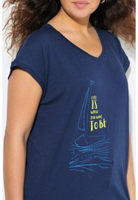 Marinblå t-shirt med V-ringning, korta ärmar som har ett grafik av en segelbåt och vågor, tillsammans med text i gult och blått. Mjuk textur.