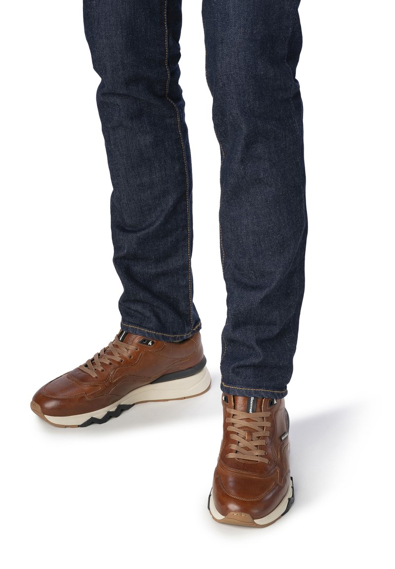 Baskets en cuir marron avec des accents beige, une semelle épaisse et des lacets. Portées avec un jean en denim bleu marine à coupe classique.