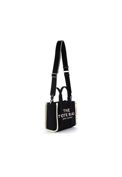 Bolsa tote retangular preta com acabamentos brancos, alças curtas, correia de ombro ajustável e texto "THE TOTE BAG MARC JACOBS" na frente.