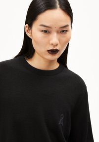 Schwarzer Strickpullover mit rundem Halsausschnitt und einem dezenten Logo auf der linken Brust. Verfügt über eine glatte Textur und eine figurbetonte Silhouette.