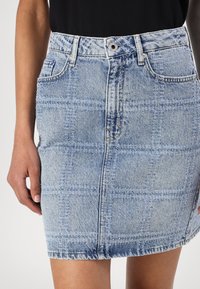 Denim krilo v svetlo modri barvi s karirastim vzorcem. Ima prilegajoč pas, sprednje zapiranje na gumb in dva stranska žepa.