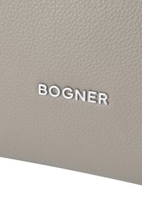 Jasno beżowa skórzana torba z teksturą, z wyraźnym srebrnym logo "BOGNER" wytłoczonym na powierzchni. Gładki i elegancki design.