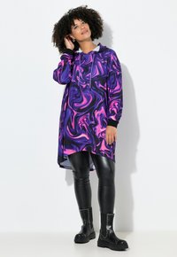 Paarse en roze gedraaide hoodie-jurk met lange mouwen, zijsplitten en zwarte accenten, gecombineerd met zwarte leren leggings en gestudeerde enkellaarsjes.