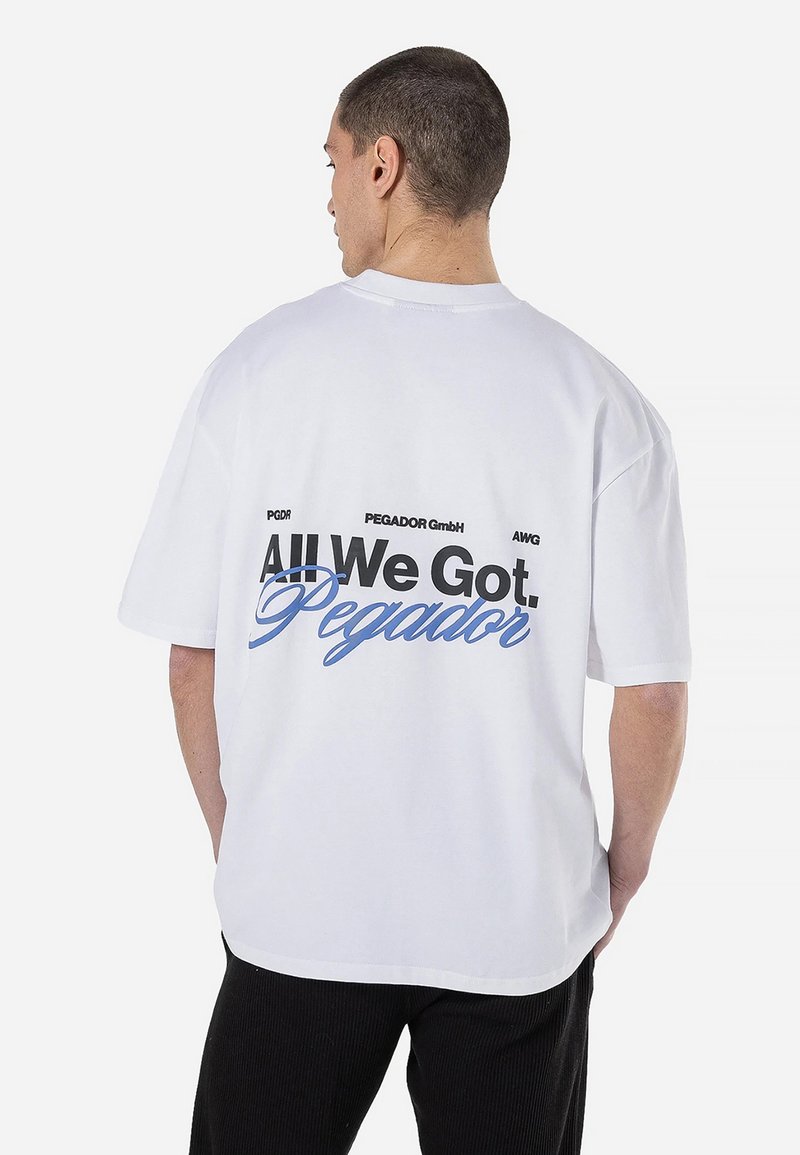 Balta trumpomis rankovėmis marškinėliai su dideliu juodu ir mėlynu užrašu ant nugaros, kuriame ryškiai išreikšta frazė "All We Got. Pegador."