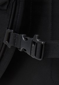 Boucle latérale en plastique noir fixée sur une sangle en nylon noir réglable sur un fond en tissu noir.